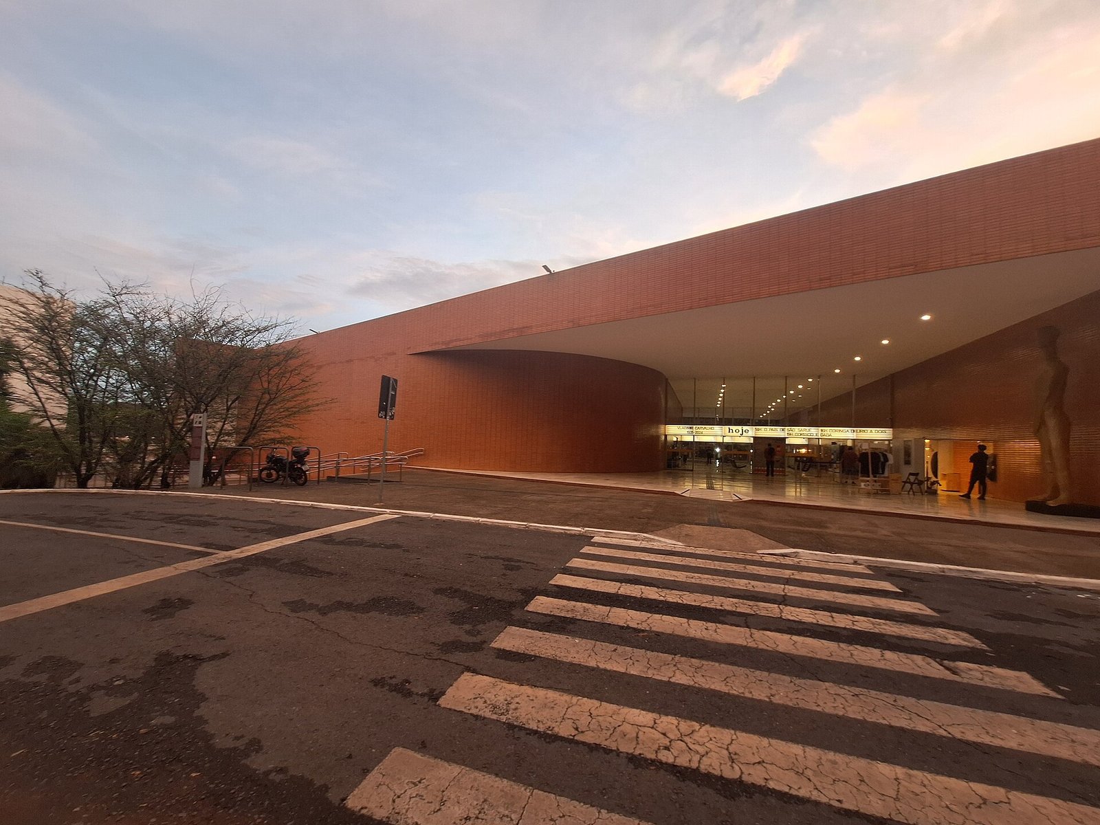 Fachada do Cine Brasília ao entardecer, com a marquise iluminada e a programação do dia