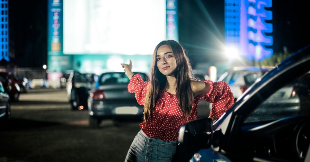 Carros estacionados de frente para a tela iluminada de um cinema drive-in à noite