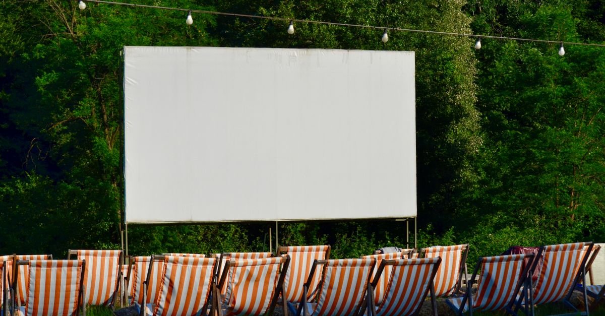Tela de cinema ao ar livre com fileiras de cadeiras de praia listradas em frente