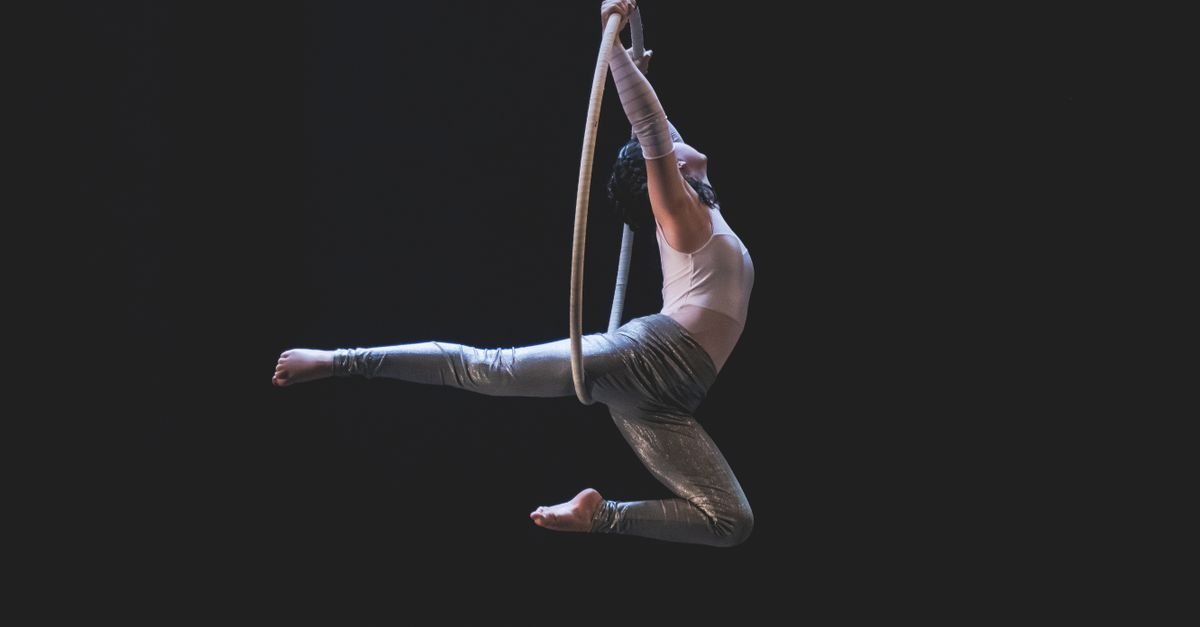 Artista de circo em apresentação de lira aérea sobre fundo escuro