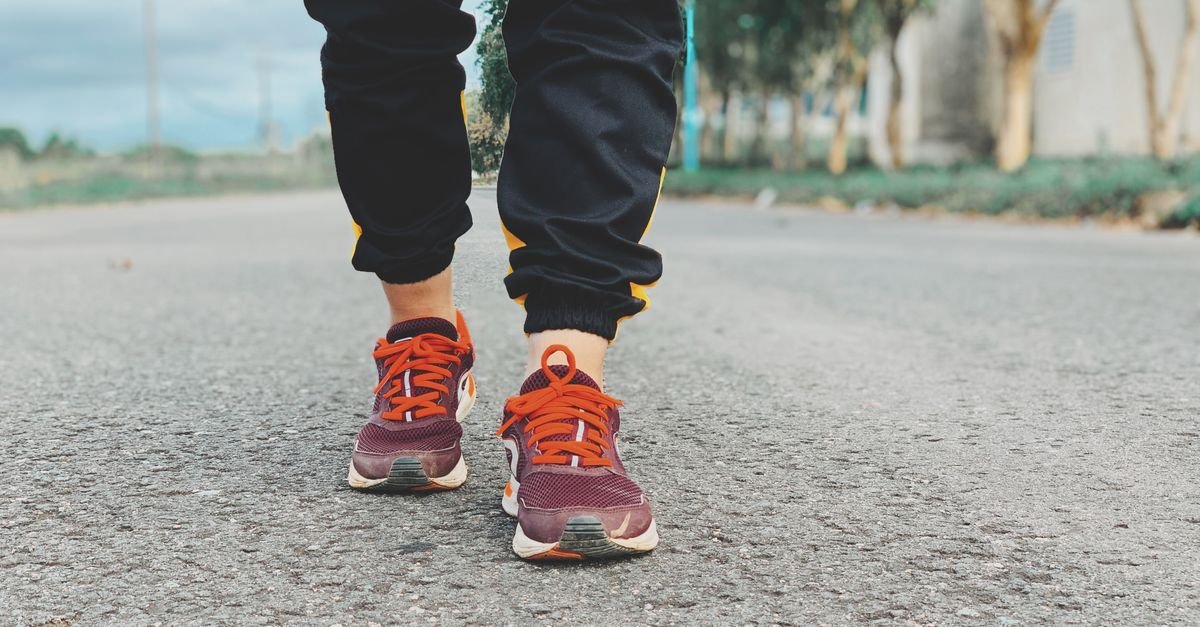 Pés de corredor com tênis esportivos sobre o asfalto de uma via arborizada