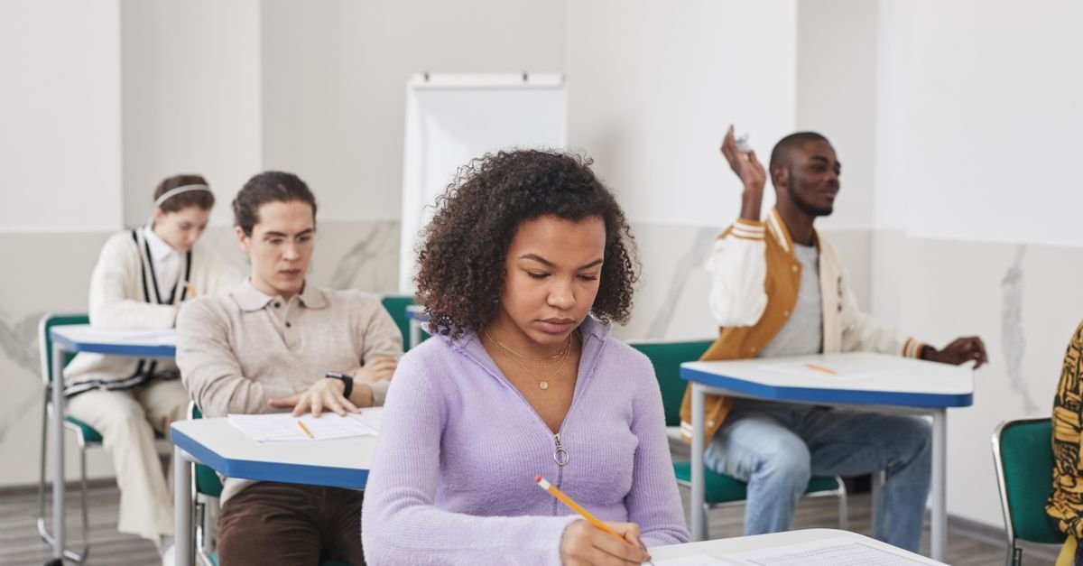 Estudantes sentados em carteiras fazendo prova em sala de aula