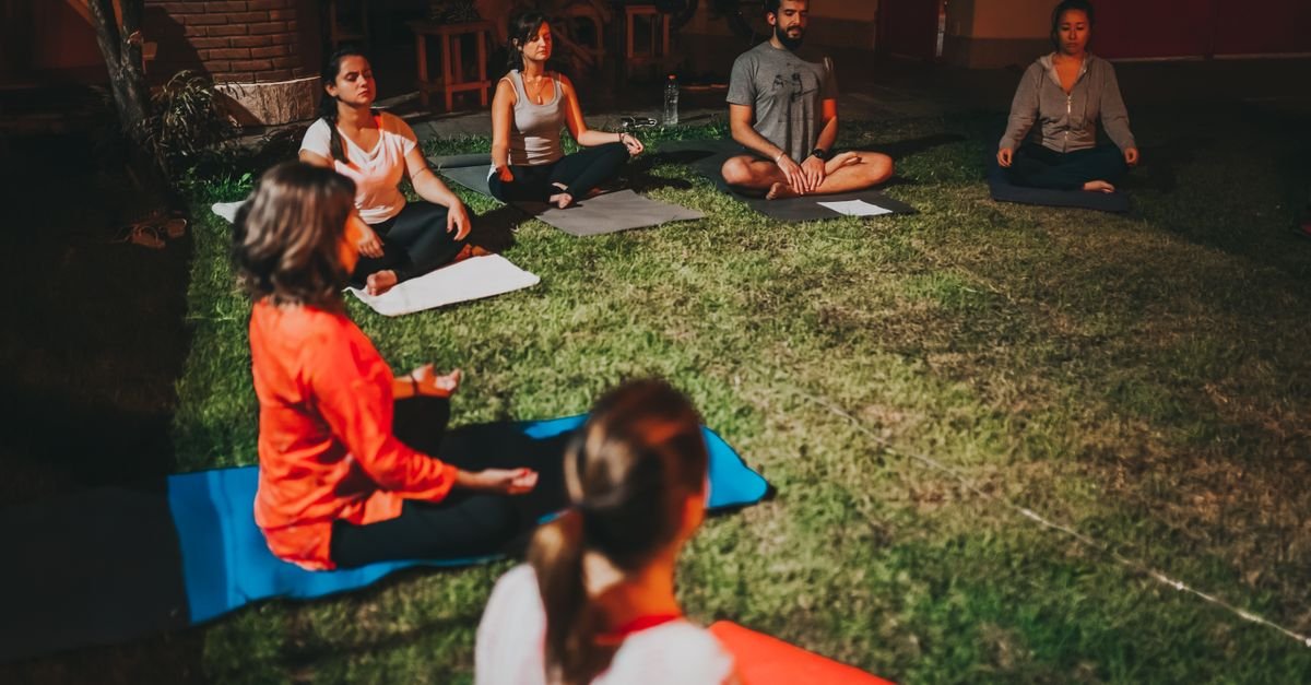 Grupo de pessoas sentadas em tapetes praticando meditação ao ar livre sobre gramado