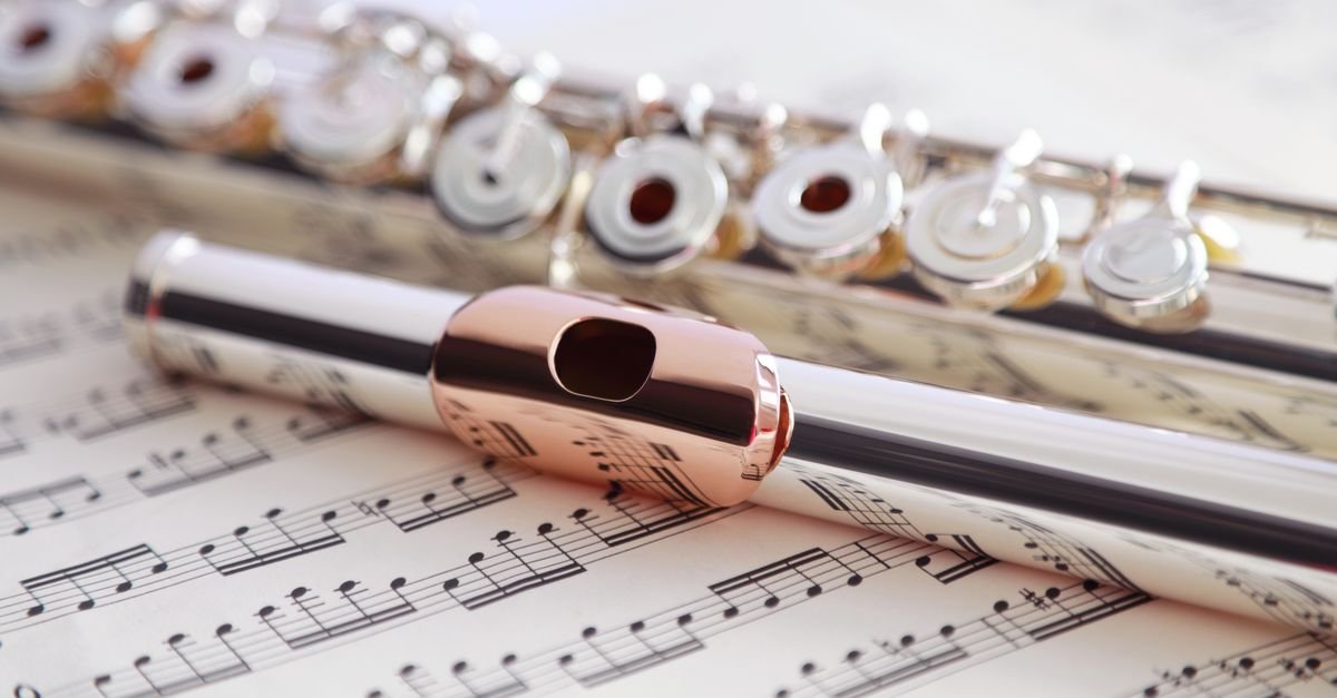 Flauta transversal prateada apoiada sobre partitura de música impressa