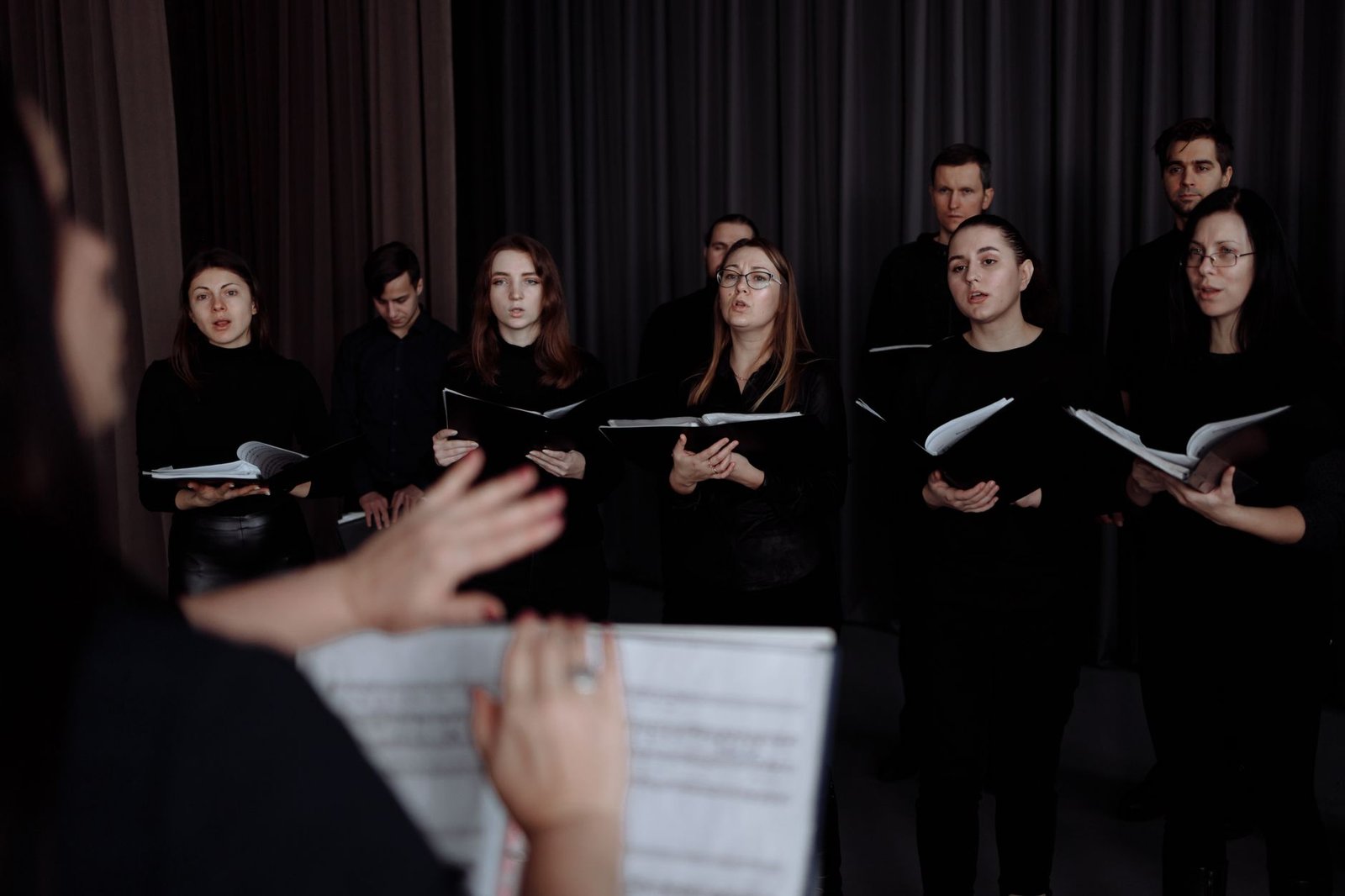 Coralistas de preto cantam com partituras nas mãos, sob a regência de uma maestrina (foto de arquivo, não é do Cantus Firmus)
