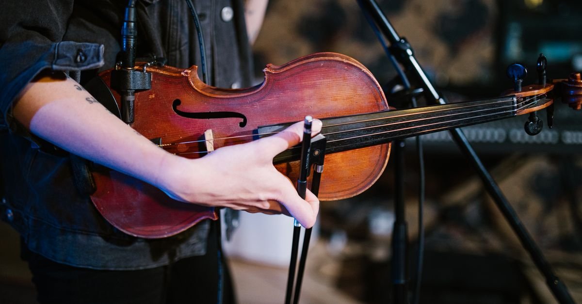 Mãos de um violinista com o arco sobre as cordas de um violino diante de um microfone