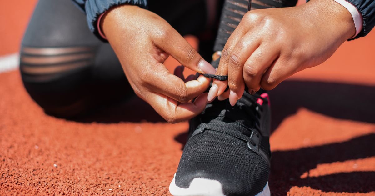Corredora amarra o cadarço do tênis em pista de atletismo antes de treino