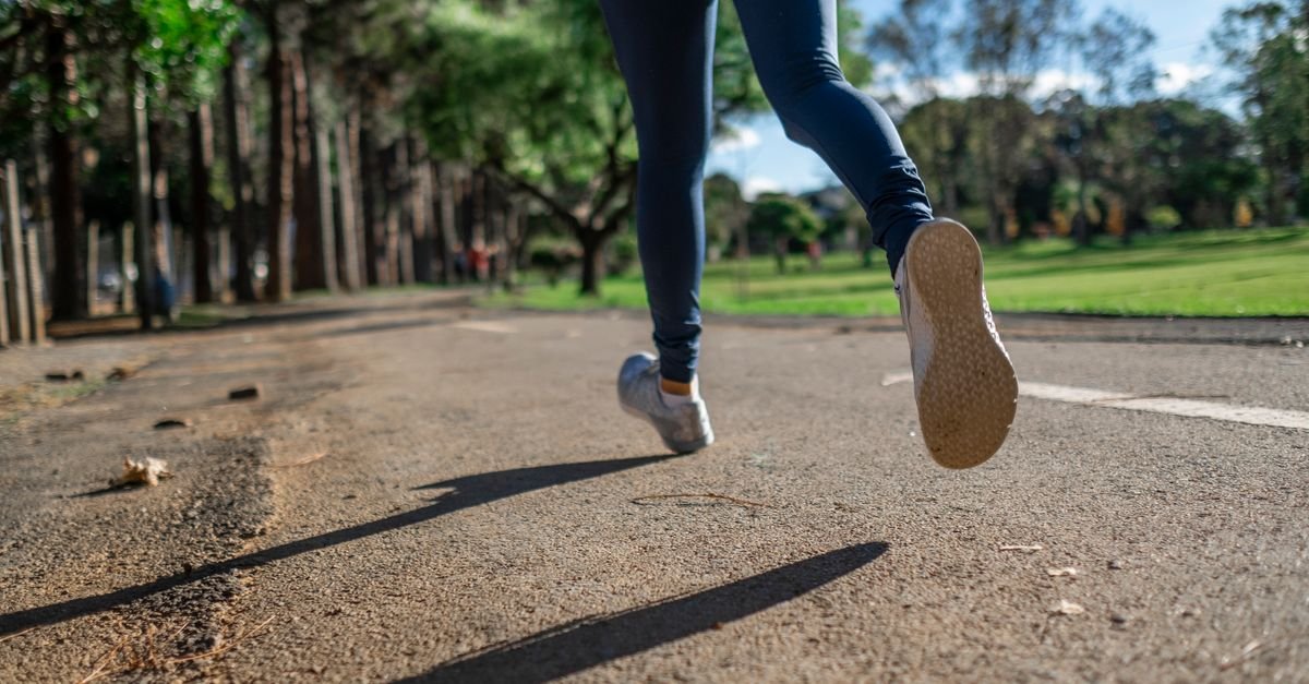 Pernas de uma corredora em movimento numa via de parque arborizado