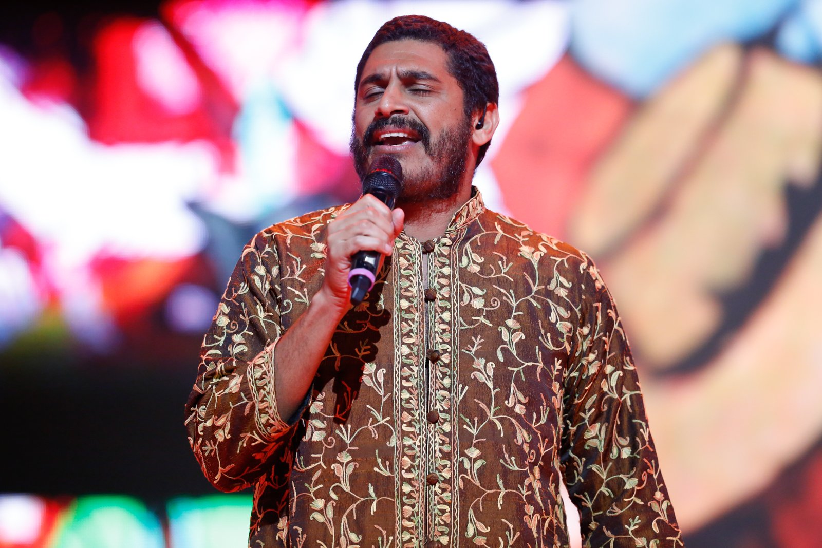 Criolo canta ao microfone, de camisa bordada em tons de marrom, durante o Prêmio da Música Brasileira de 2014