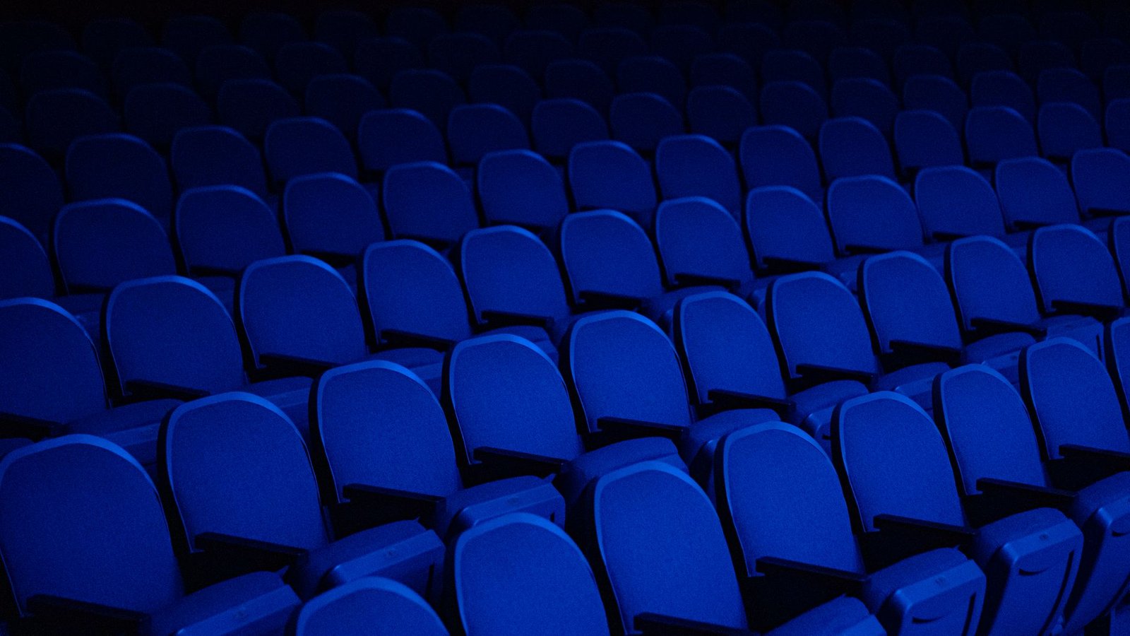 Fileiras de poltronas azuis vazias em um teatro com iluminação baixa