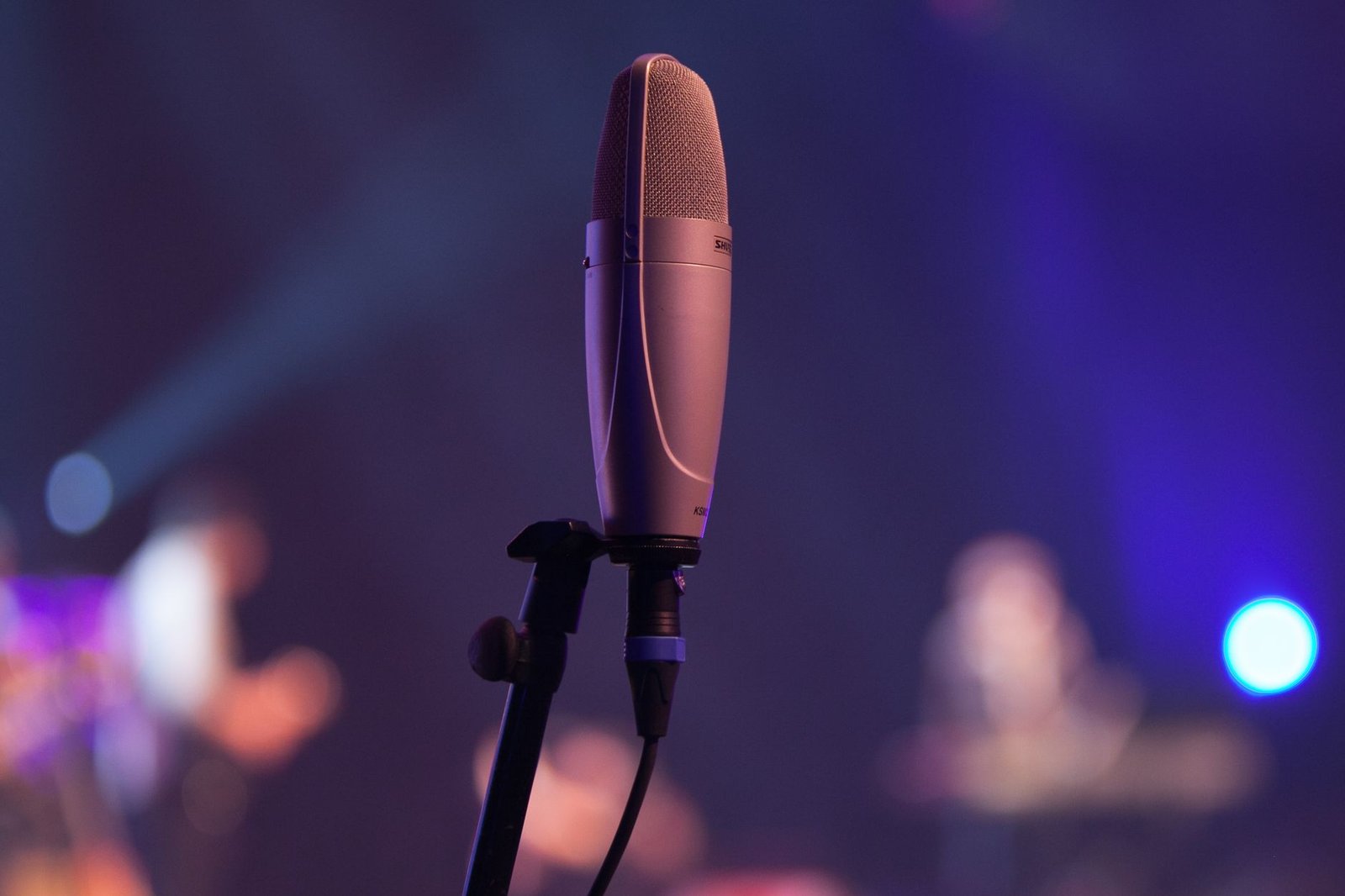 Microfone de estúdio sobre pedestal com luzes de palco desfocadas ao fundo