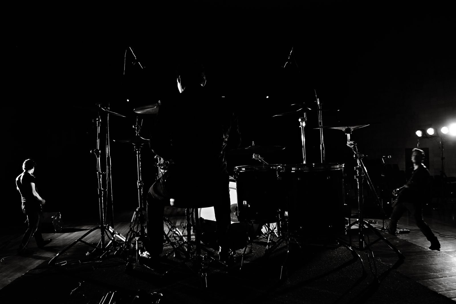 Silhueta de baterista e dois músicos em palco escuro, em foto de banco de imagens, sem relação com o show
