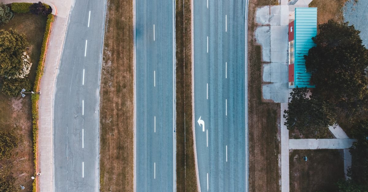 Vista aérea de pista asfaltada de mão dupla, vazia, com faixas e seta de conversão pintadas
