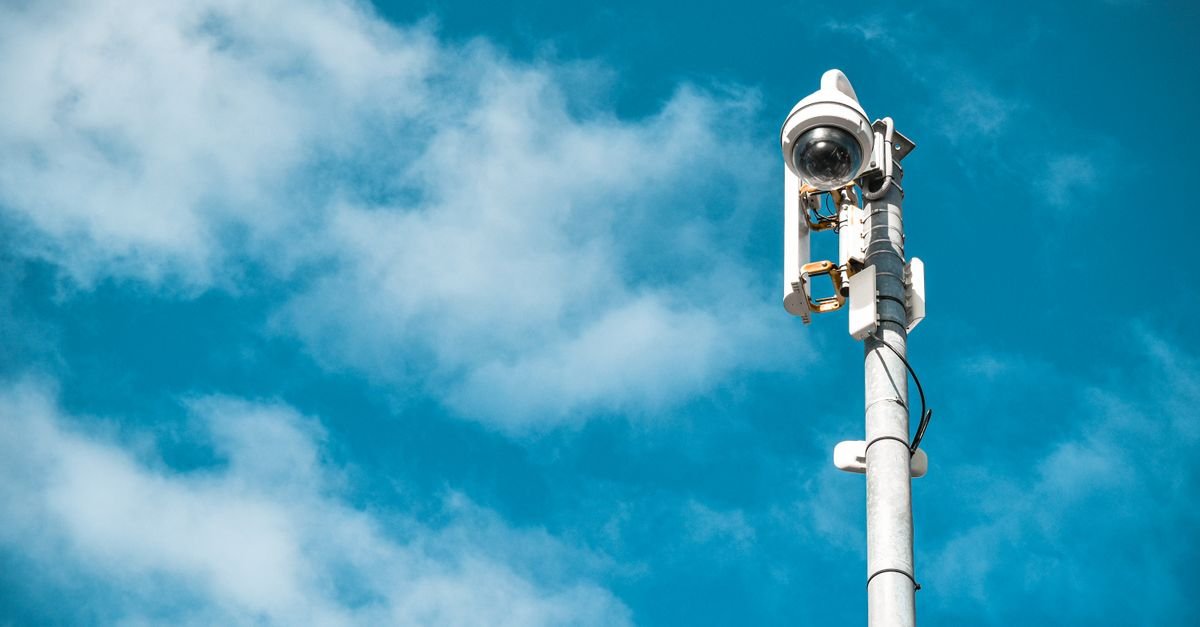 Câmera de videomonitoramento instalada no alto de um poste, com o céu azul ao fundo
