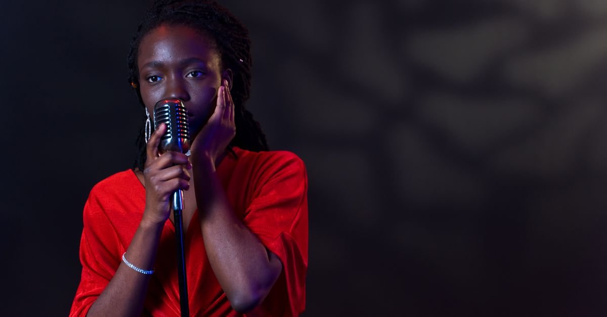 Cantora de vestido vermelho com as mãos no microfone de palco sob luz azul