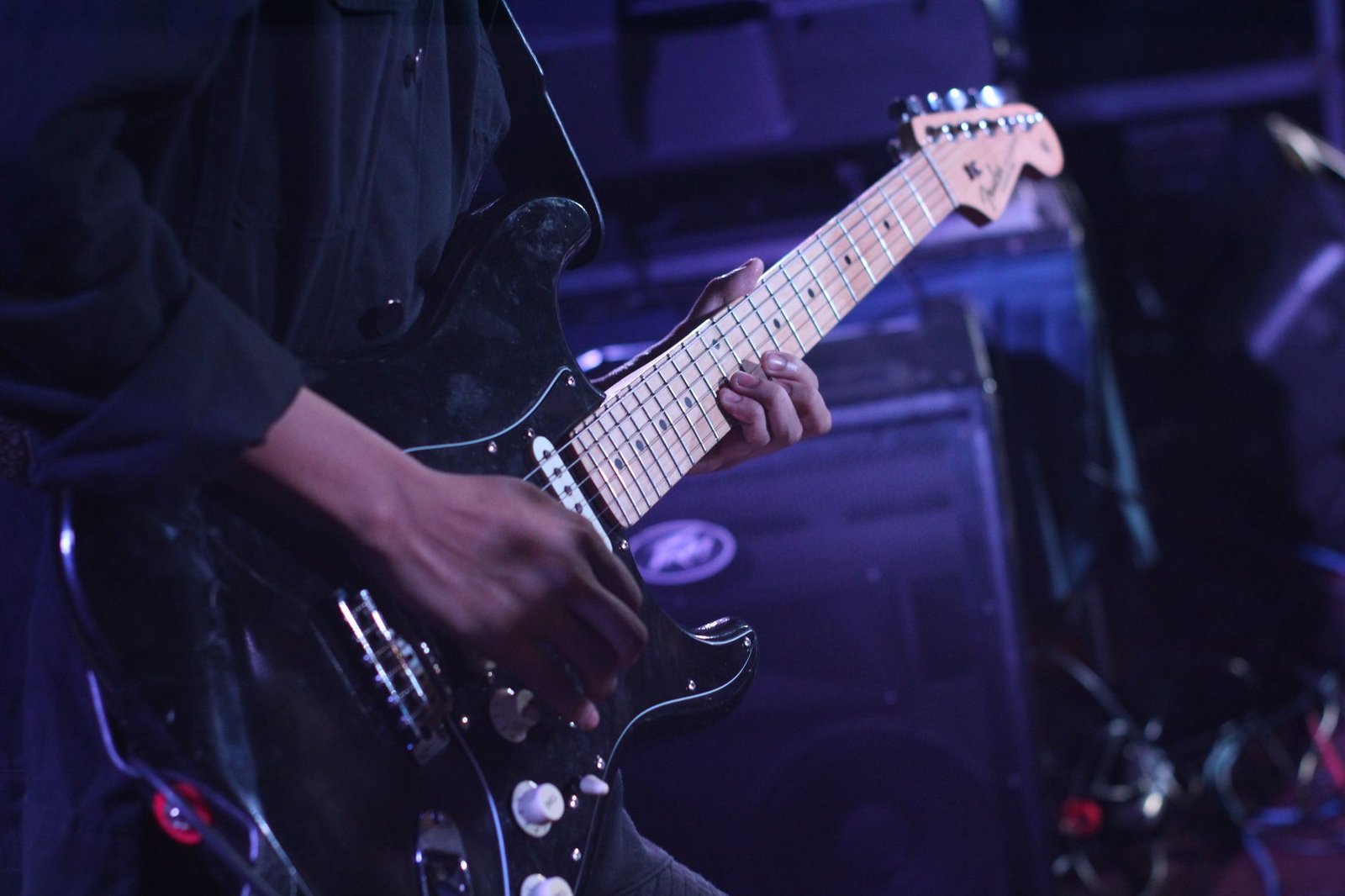 Guitarrista toca guitarra elétrica preta sob luz azul em palco de casa de shows