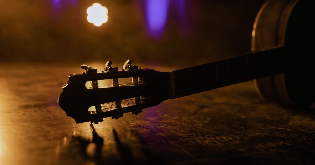 Braço de violão em close com luzes de palco ao fundo