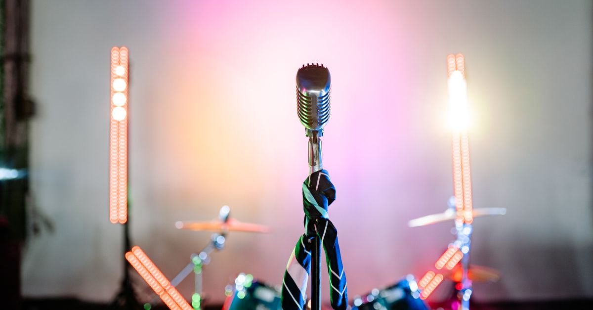Microfone retrô em pedestal no palco com luzes coloridas e bateria ao fundo
