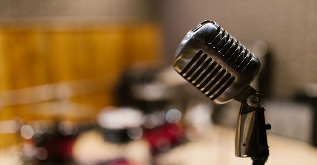 Microfone vintage cromado em estúdio, com bateria desfocada ao fundo