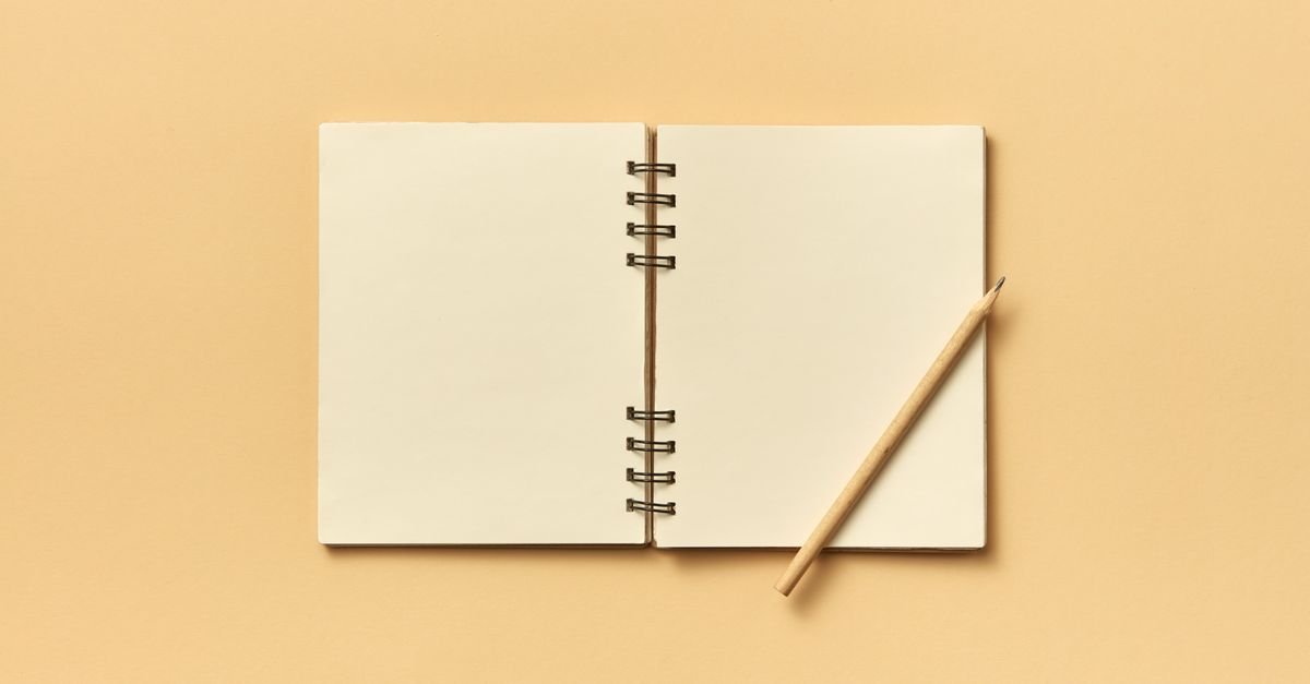 Caderno espiral aberto com folhas em branco e um lápis apoiado, sobre fundo bege