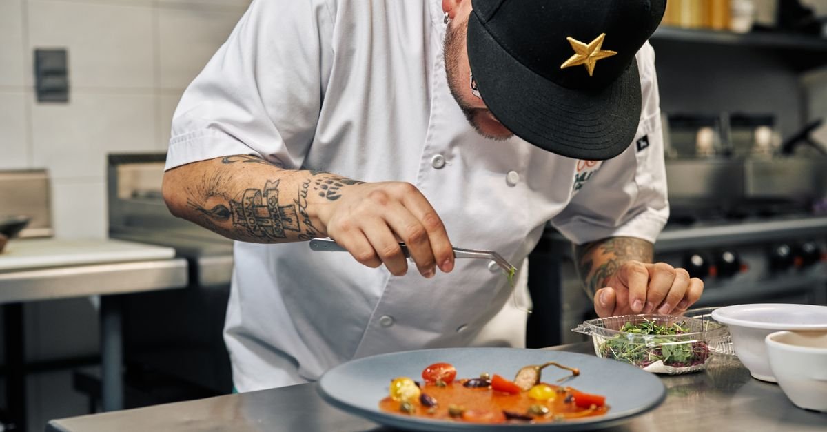 Cozinheiro finaliza a montagem de um prato com pinça em cozinha profissional