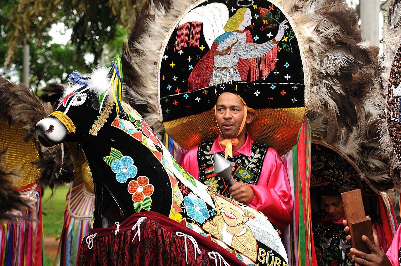 Brincante de bumba meu boi com chapéu bordado ao lado do boi ornamentado em apresentação de cultura popular em Brasília