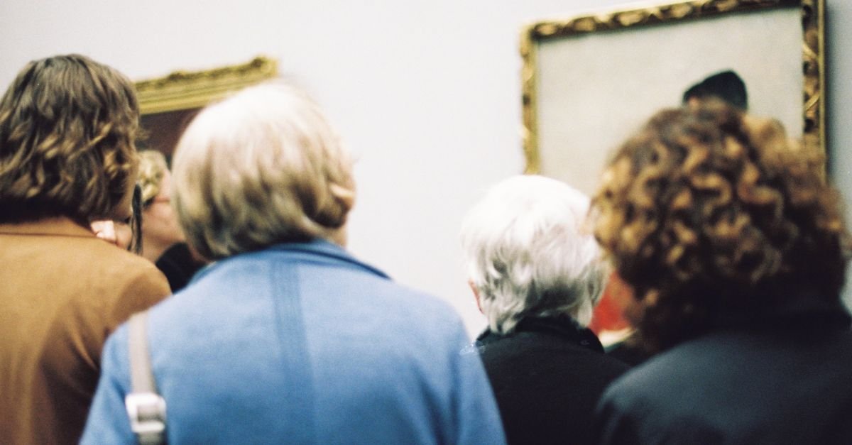 Grupo de visitantes de costas observando um quadro emoldurado em uma exposição