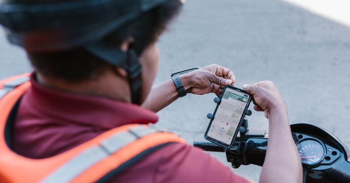 Entregador de colete laranja consulta um aplicativo de mapa no celular preso ao guidao da moto