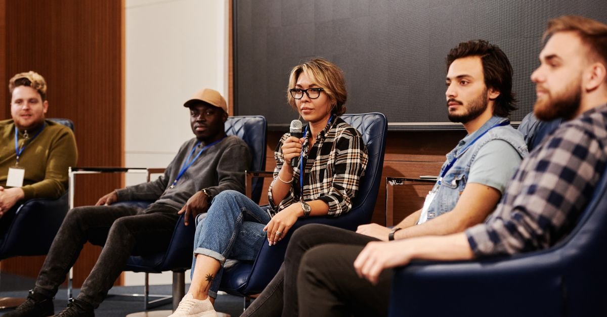 Participantes de um painel de debate sentados no palco de um evento fechado