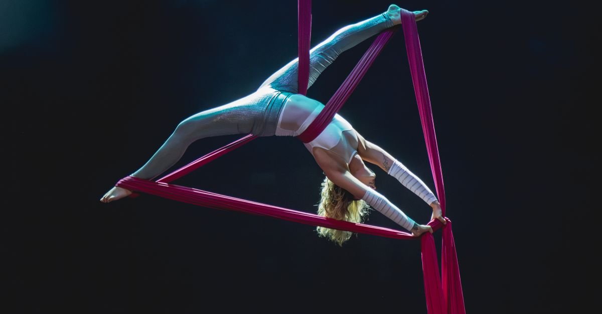 Artista de circo suspensa em tecido acrobático rosa durante apresentação