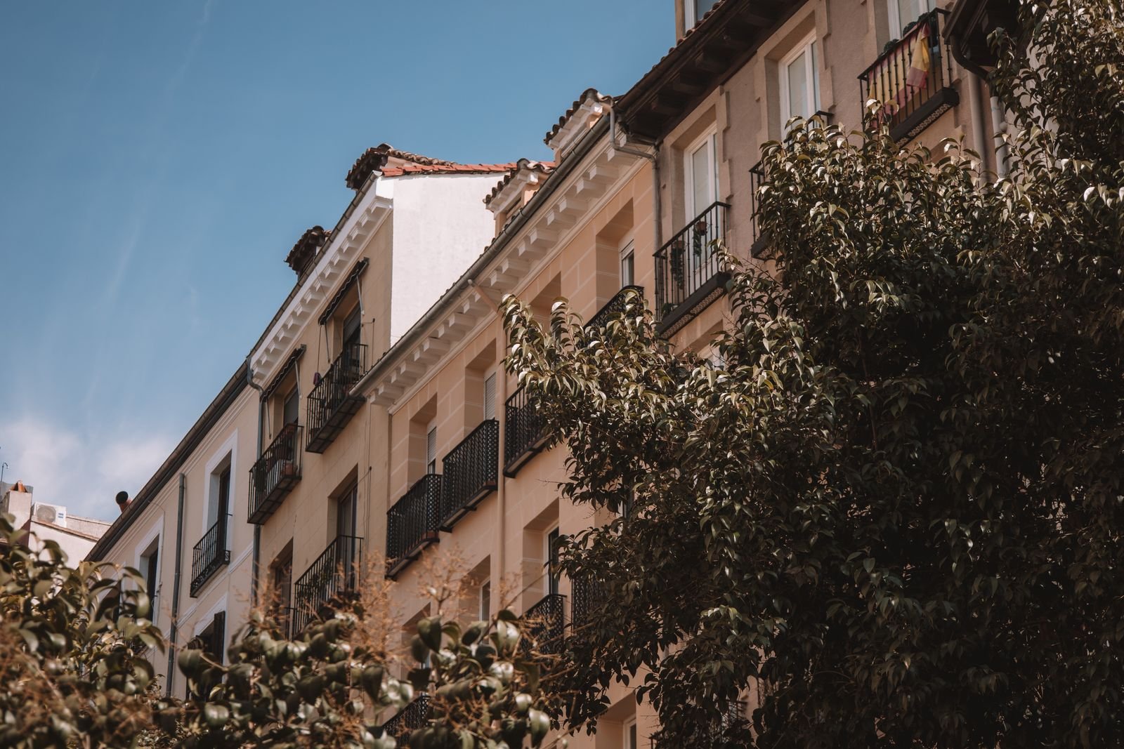 Fachada de prédio residencial com varandas e árvores sob céu azul, imagem de arquivo