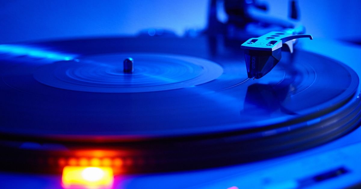 Disco de vinil girando em toca-discos sob luz azul, com a agulha apoiada no sulco