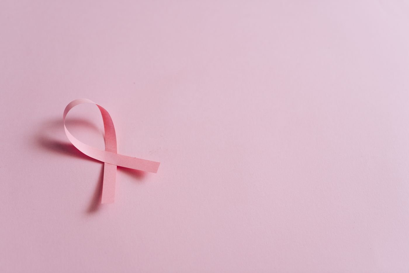 Laço rosa de papel sobre fundo rosa, símbolo da campanha contra o câncer de mama