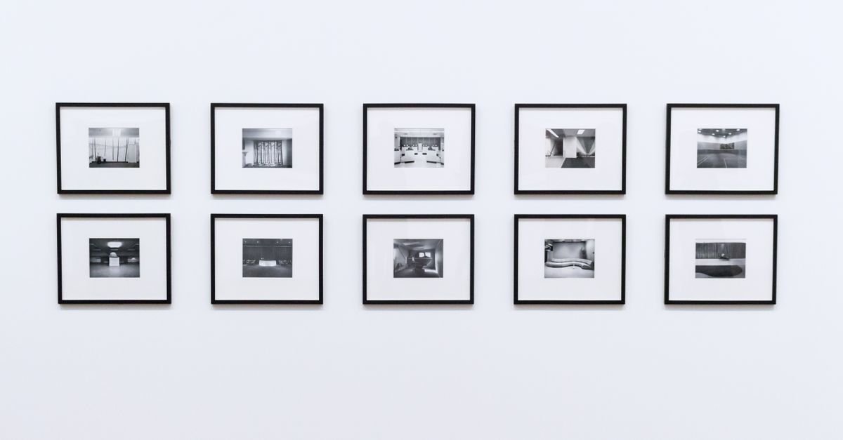 Parede branca de galeria com dez fotografias em preto e branco emolduradas, dispostas em duas fileiras