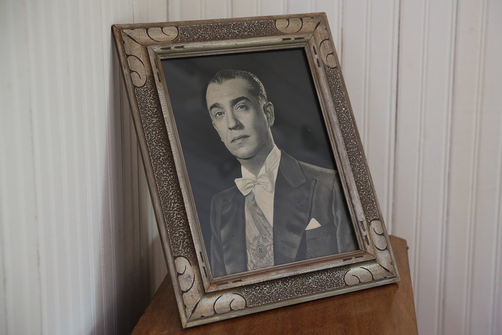 Retrato emoldurado de Juscelino Kubitschek com a faixa presidencial, apoiado sobre um móvel de madeira