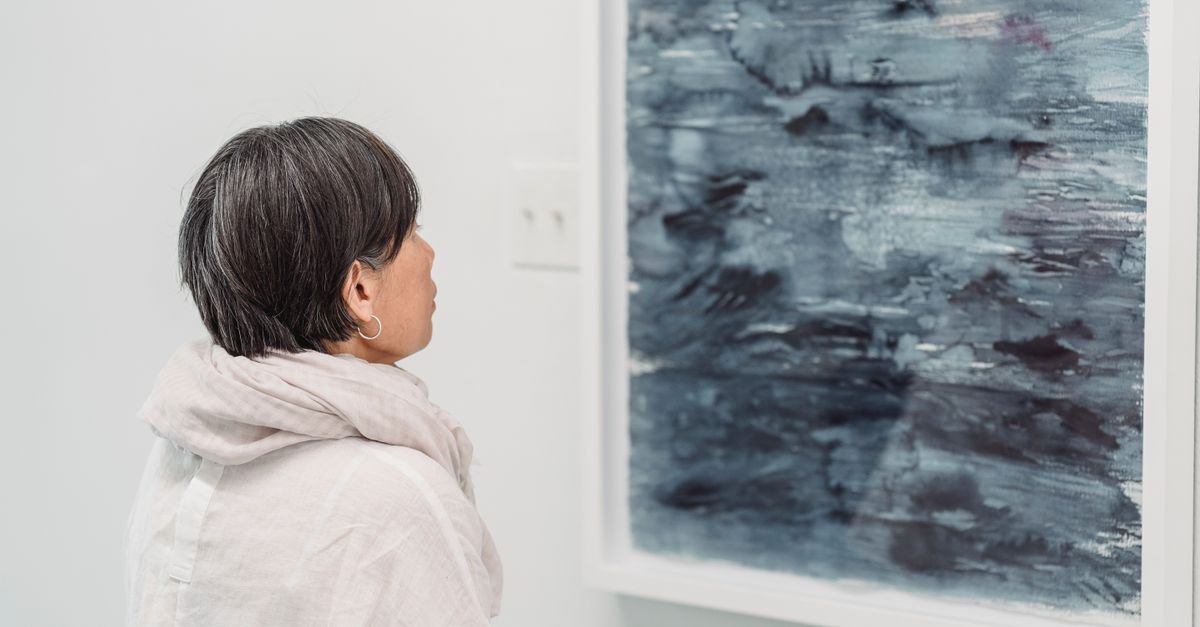 Visitante observa uma pintura abstrata emoldurada em parede branca de galeria de arte