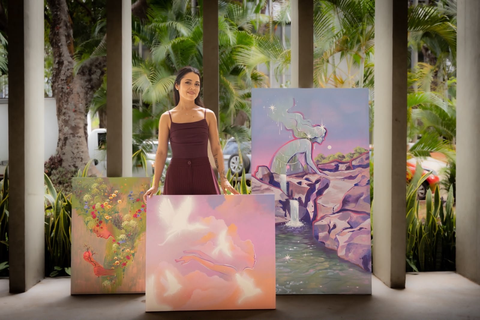 A artista Camilla Siren entre três pinturas de sua exposição Fantasia Concreta