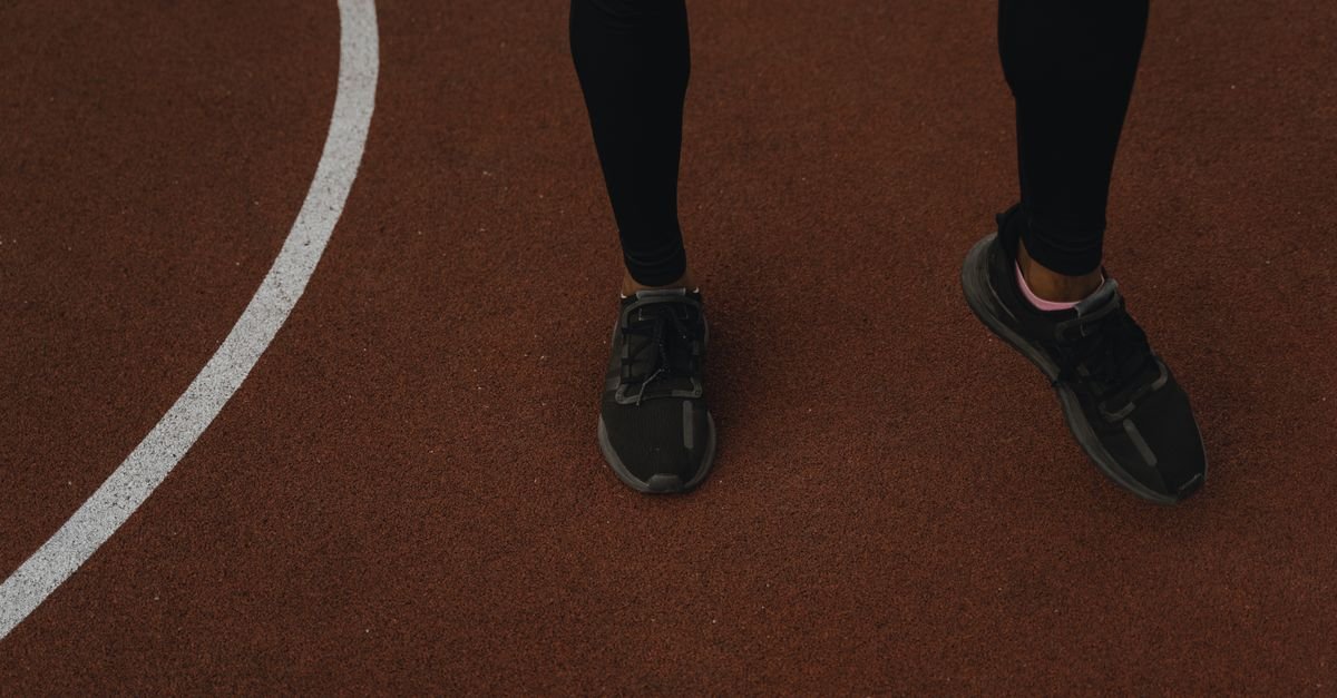 Pernas e tênis de corredor sobre a pista de atletismo, em imagem ilustrativa de corrida de rua