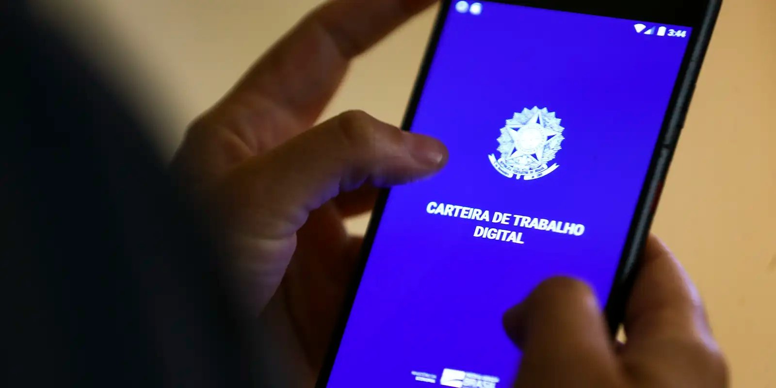 Mãos seguram celular com a tela inicial do aplicativo Carteira de Trabalho Digital
