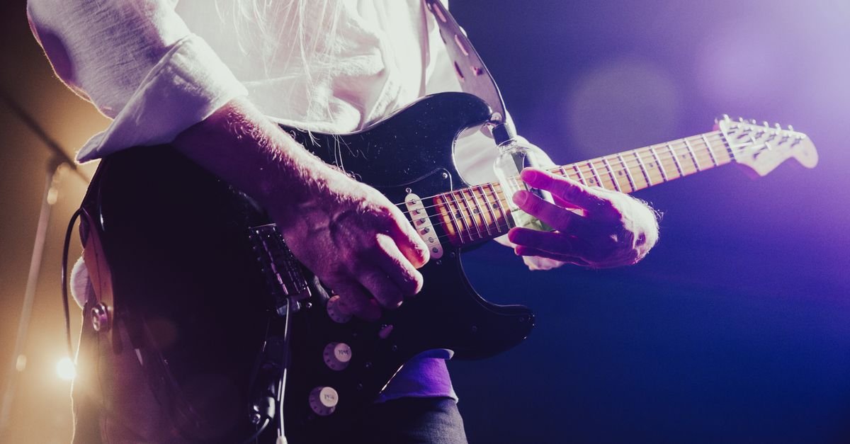 Músico tocando guitarra elétrica sob luzes roxas de palco durante show
