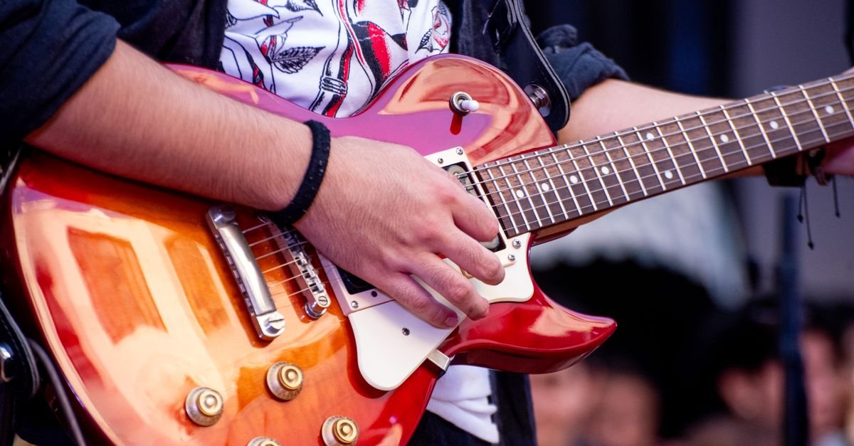 Guitarrista toca guitarra elétrica vermelha durante show ao ar livre