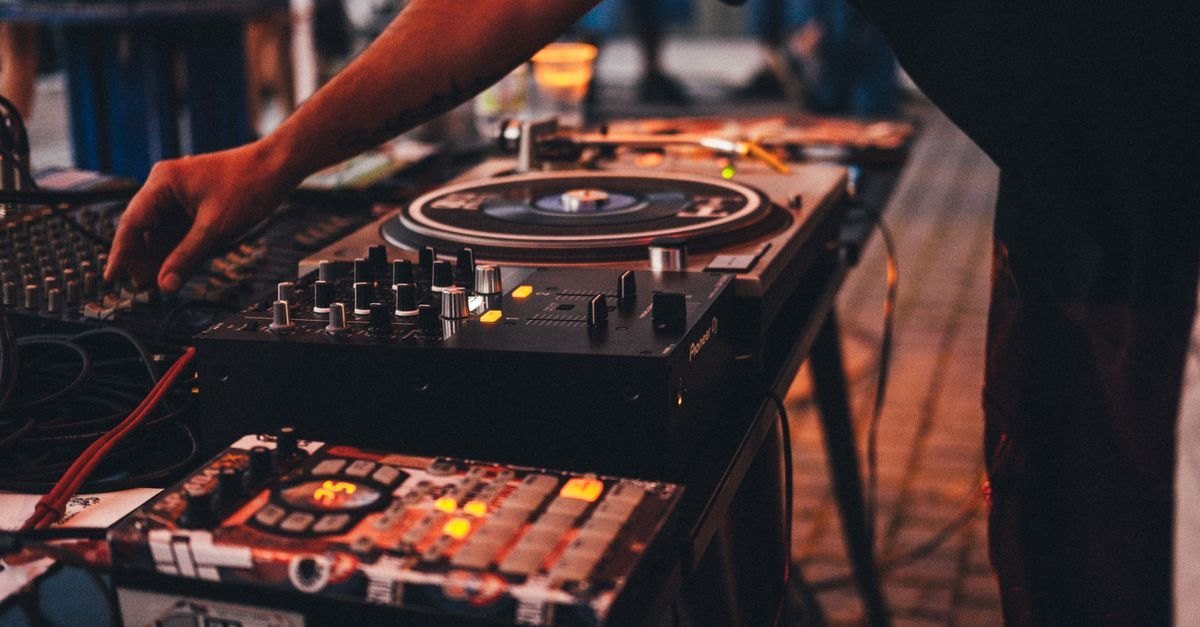 Toca-discos e mesa de mixagem de DJ em evento ao ar livre, com luz quente de fim de tarde ao fundo