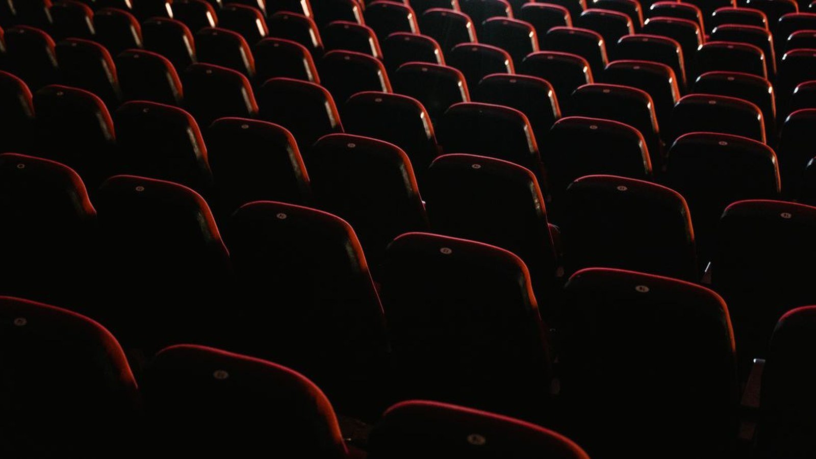 Fileiras de poltronas vermelhas vazias em sala de cinema com pouca luz