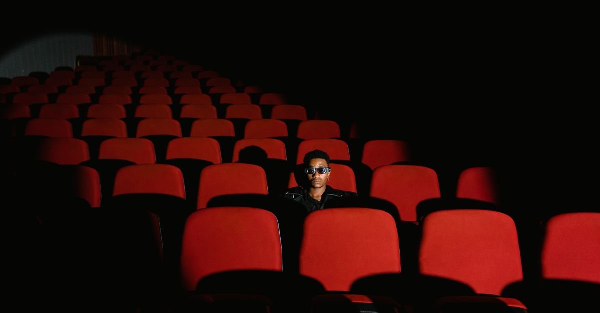 Sala de cinema com poltronas vermelhas e um espectador sentado ao fundo