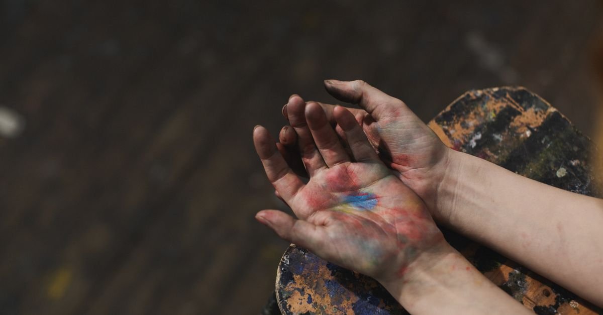 Mãos manchadas de tinta colorida apoiadas sobre paleta de pintura