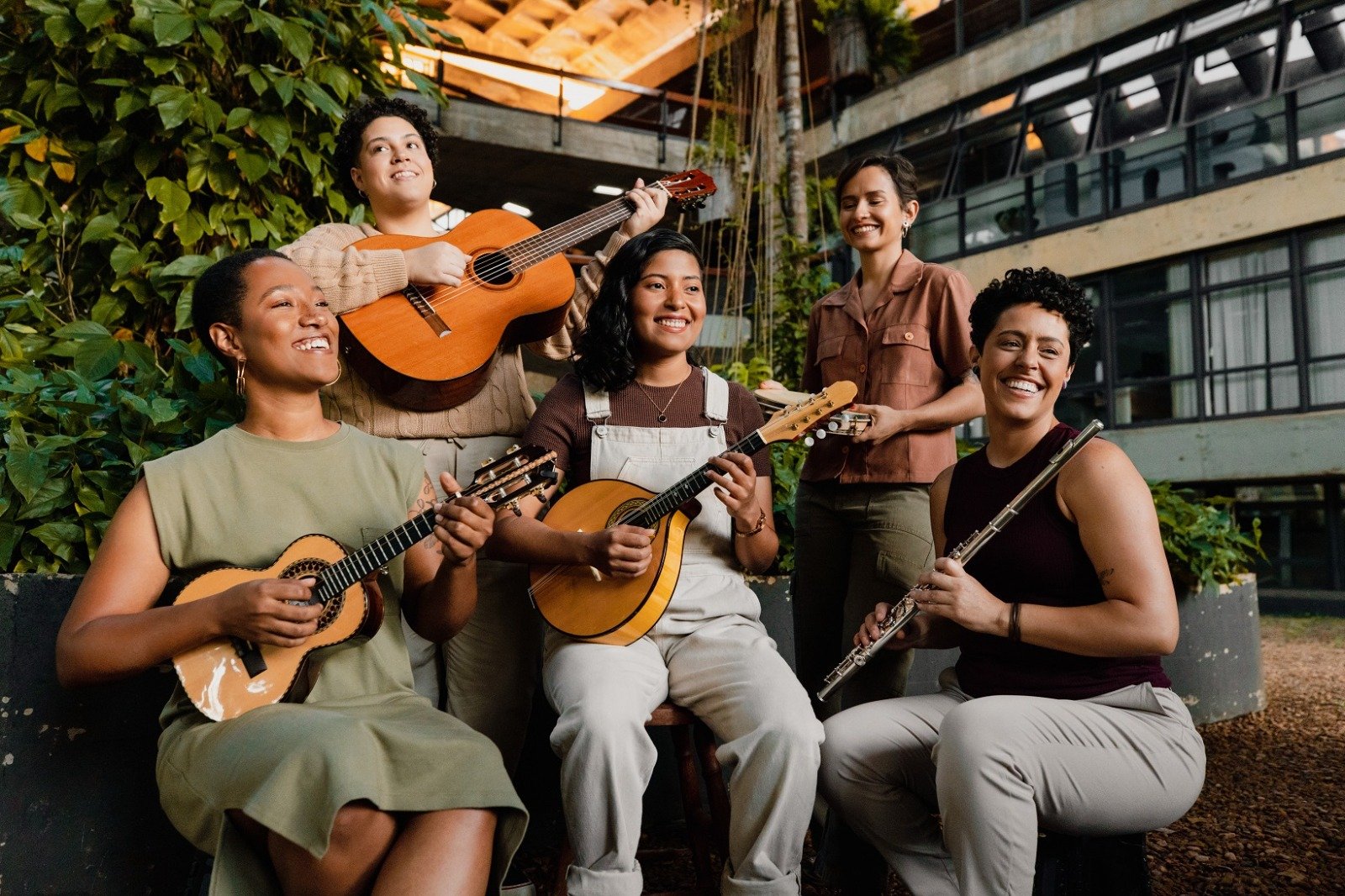 Cinco musicistas posam sorrindo com cavaquinho, violão, bandolim, pandeiro e flauta
