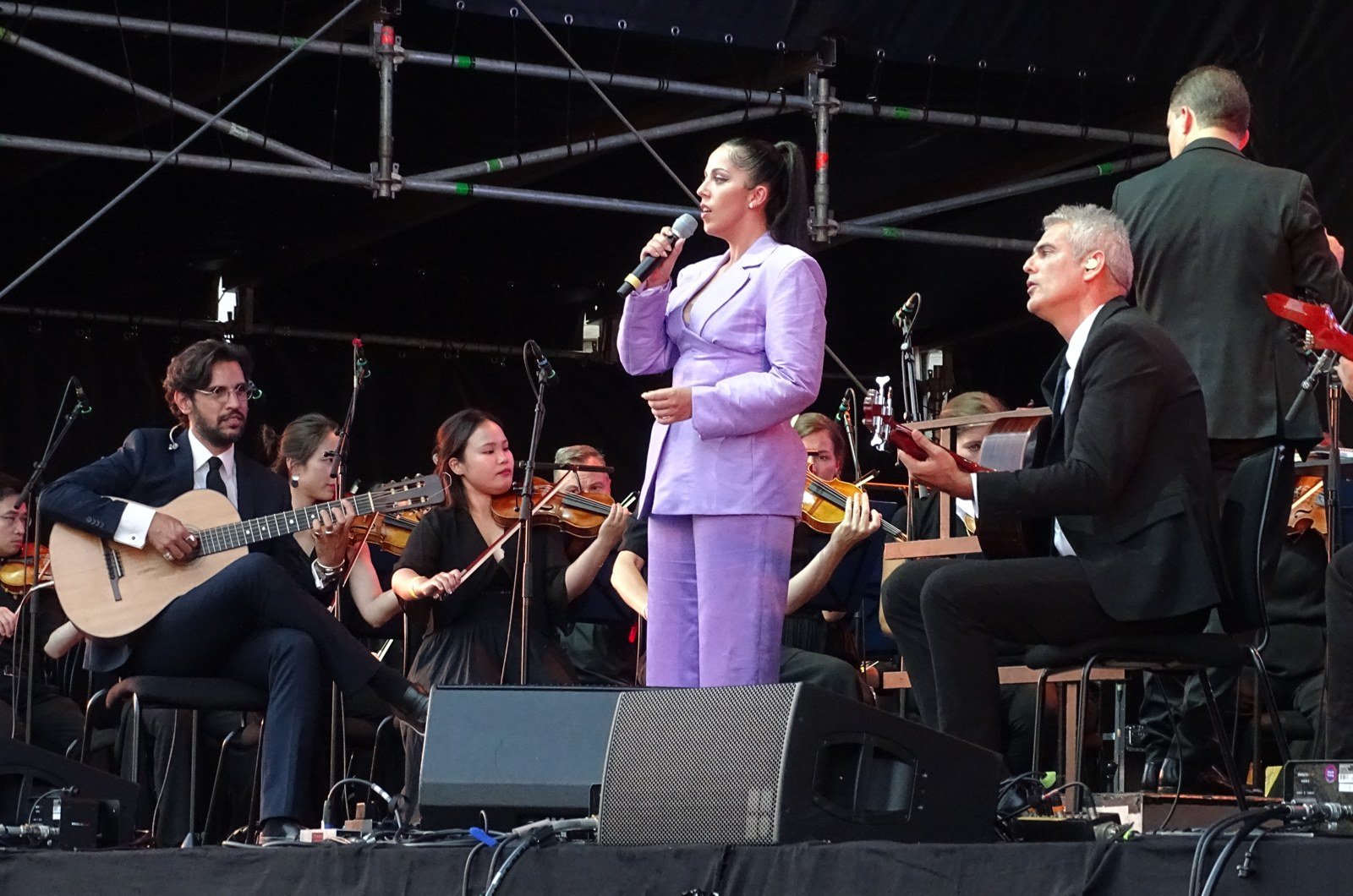 Sara Correia no palco com guitarristas e orquestra, em apresentação de 2023
