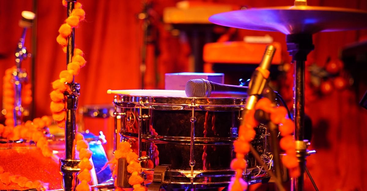 Caixa de bateria e prato de bateria montados em palco de show, com microfone posicionado sobre o instrumento