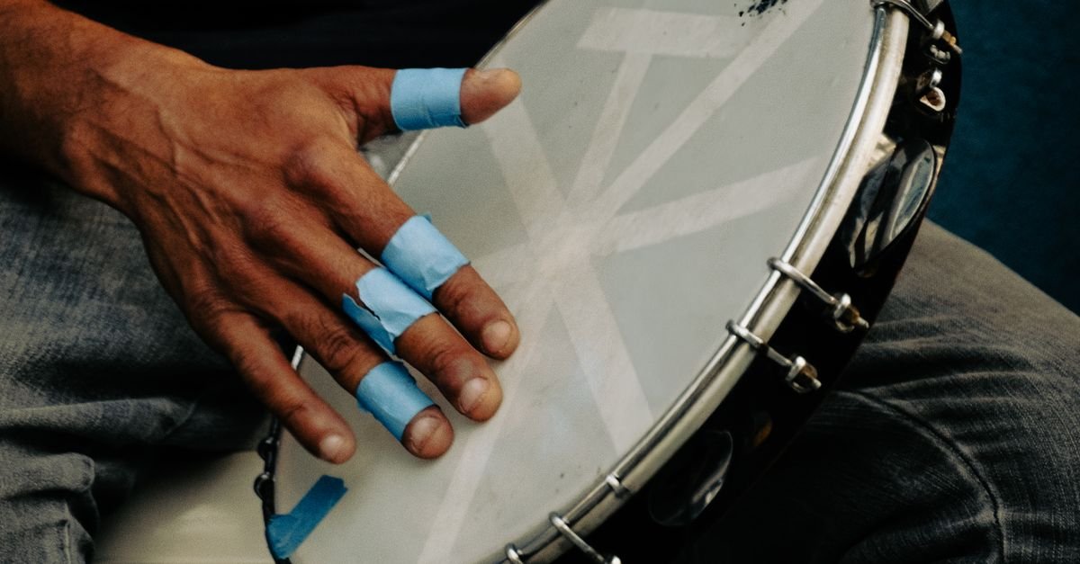 Mão com os dedos protegidos por fita azul toca um pandeiro