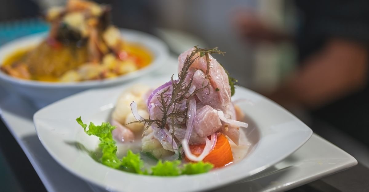 Prato de ceviche servido em louça branca com cebola roxa e folhas verdes